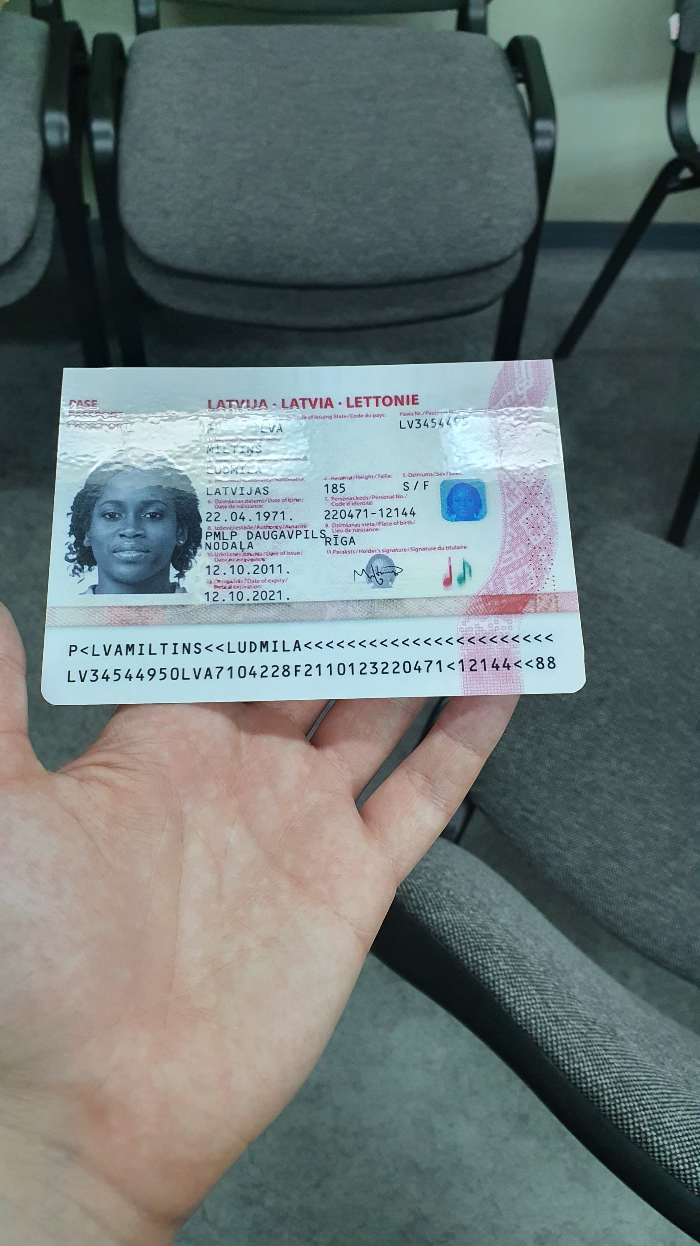 Passaporto lettone tenuto in mano, con un riflesso che cancella la riga di cognome e nome; documento fittizio del dataset MIDV-2020